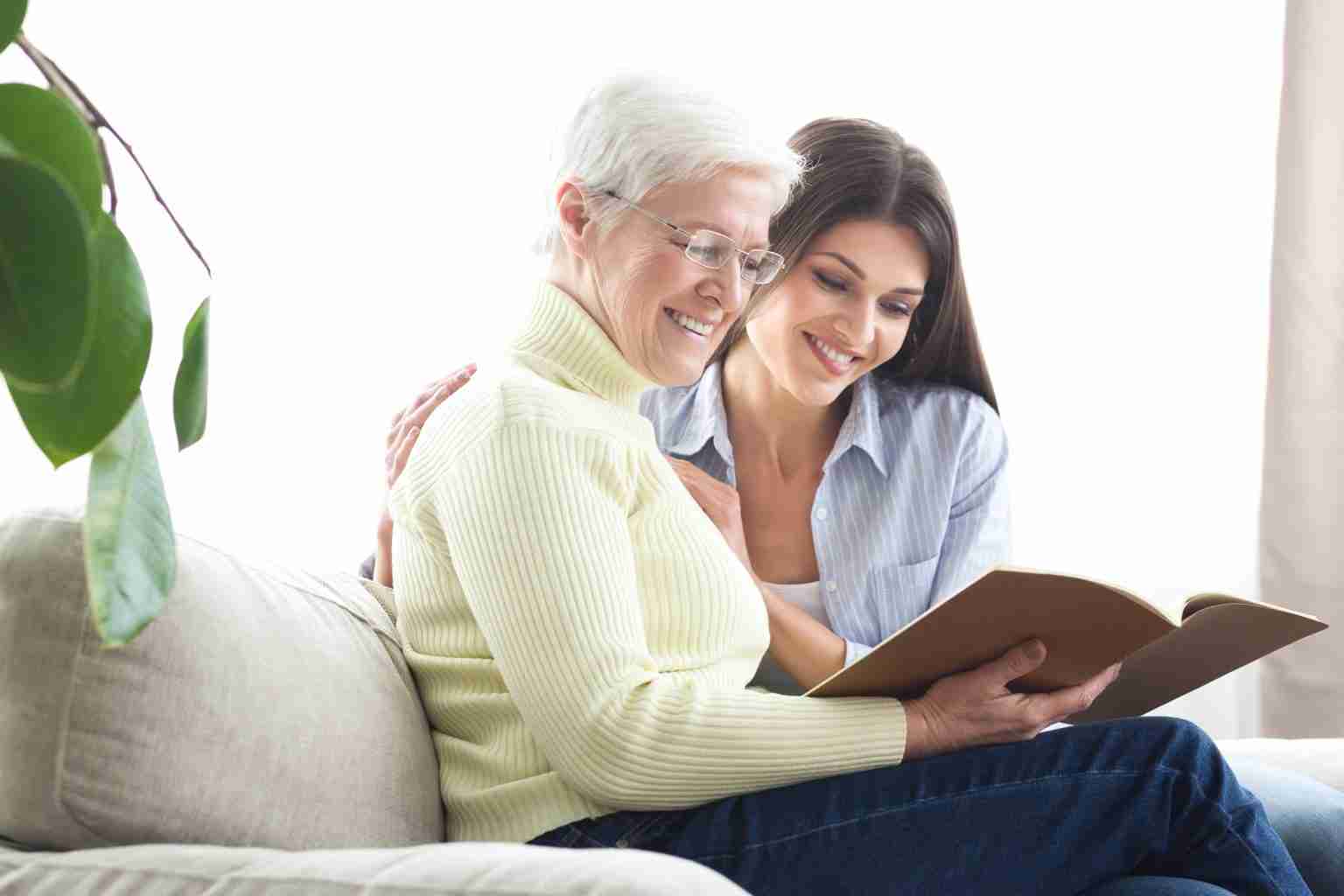 A mother and grown daughter look at a photo book together