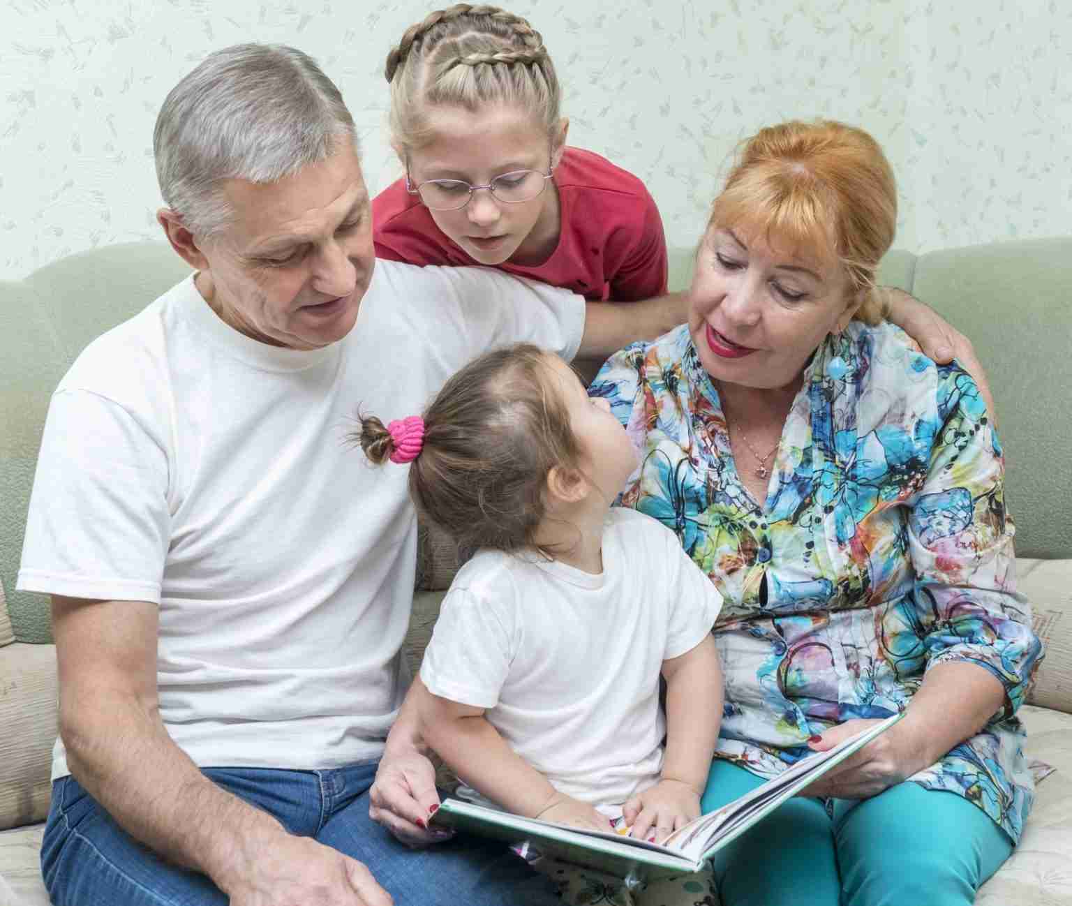 Grandmother and grandfather share a photo book with granddaughters while sitting at home on the couch