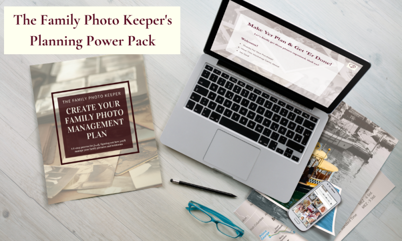 A laptop and an e-book on a desk along with photographs, eyeglasses and a phone
