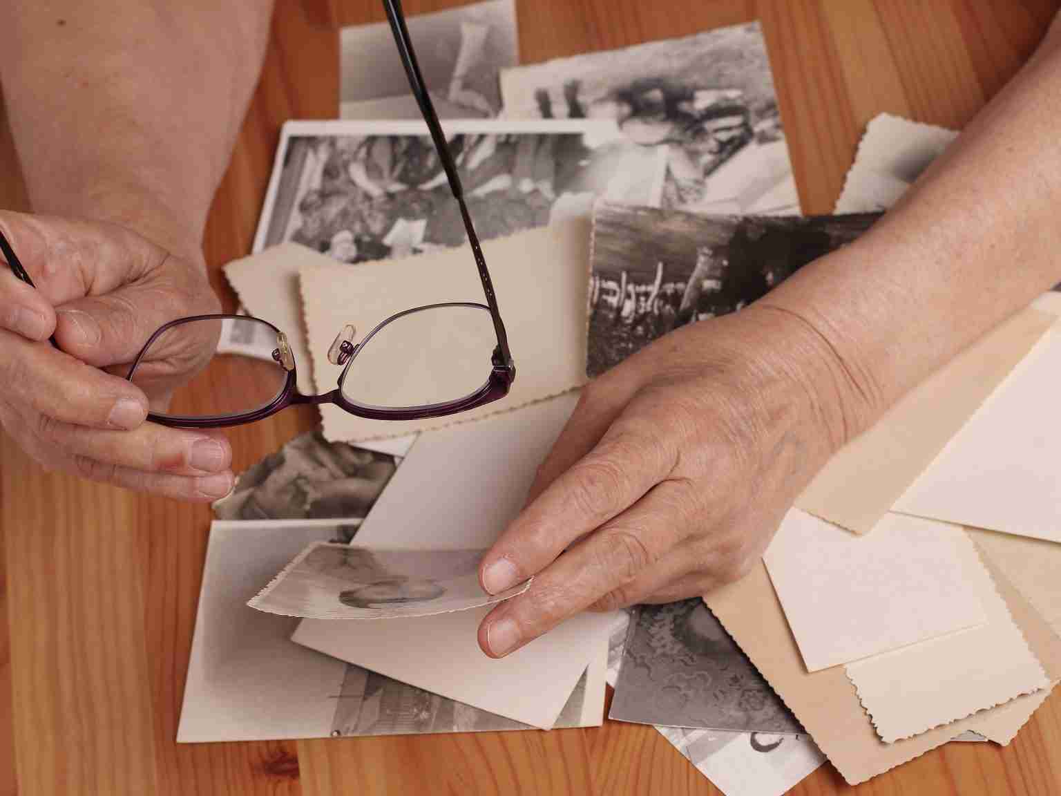 An elderly woman looks at old photographs, recalls her past youth. Hands on the table.